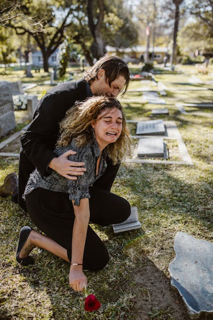 A poignant moment of grief in a sunlit cemetery with a couple mourning at a grave.